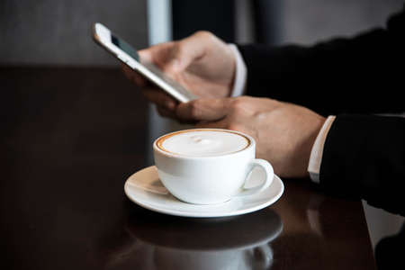 Business man using mobile phone while drinking coffee in coffee shop - modern life style business man in coffee shop conceptの写真素材