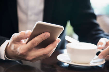 Business man using mobile phone while drinking coffee in coffee shop - modern life style business man in coffee shop conceptの写真素材