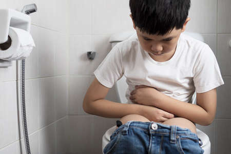 Asian boy sitting on toilet bowl - health problem concept