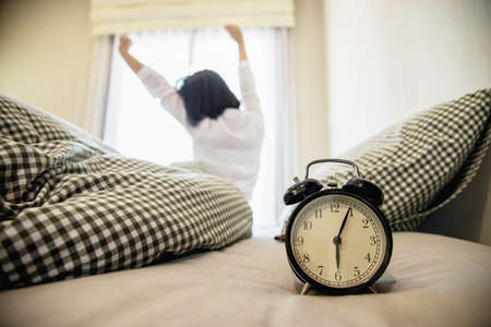 Sleepy woman reaching  holding the alarm clock in the morning with late wake up - every day life at...
