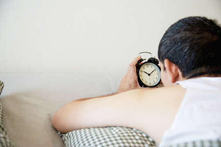 Sleepy man holding the alarm clock in the morning with late wake up - every day life at home concept