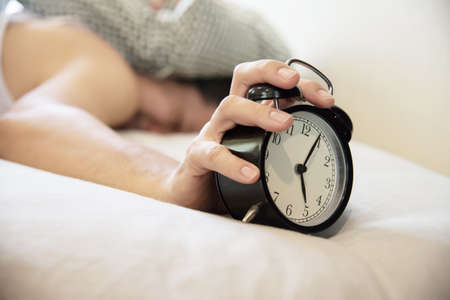 Sleepy man holding the alarm clock in the morning with late wake up - every day life at home conceptの写真素材