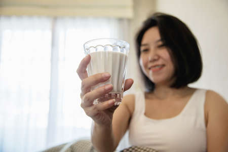 Asian woman drink milk after wake up in the morning sitting on a bed - health care conceptの写真素材