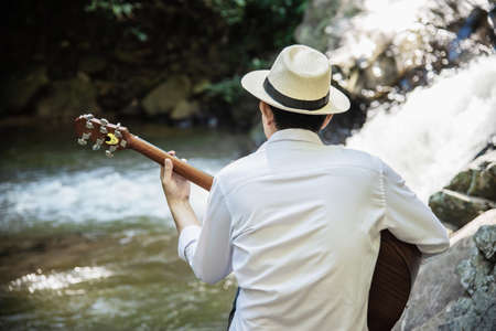 Man play guitar near to the waterfall - people and music instrument life style in nature conceptの写真素材