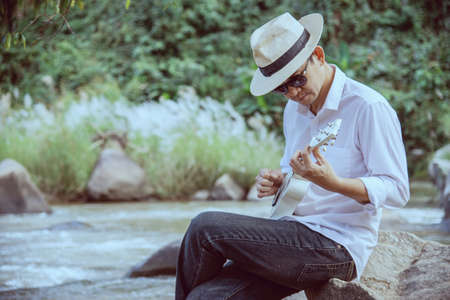 Man play ukulele new to the river- people and music instrument life style in nature conceptの写真素材