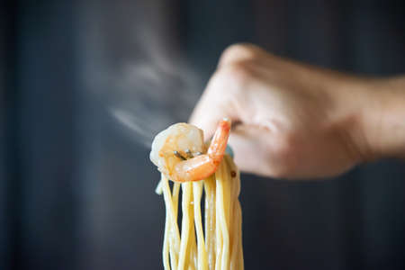 Hot and spicy spaghetti with shrimp and fork over black background - Italian food with people...
