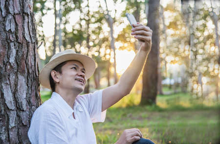 Asian man with mobile phone in forest tree nature - people in spring nature and technology concept