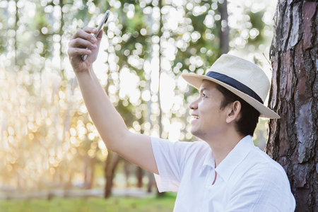 Asian man with mobile phone in forest tree nature - people in spring nature and technology conceptの写真素材