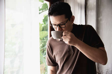 Relax Asian man drink coffee and read book in a modern style coffee shop - people with coffee cup easy lifestyle conceptの写真素材
