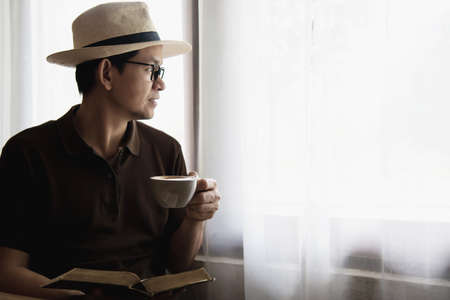 Relax Asian man drink coffee and read book in a modern style coffee shop - people with coffee cup...