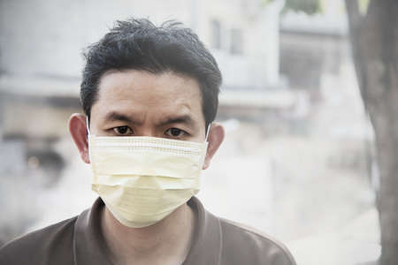 Man wearing mask protect fine dust in air pollution environment - people with protection equipment for air pollution conceptの写真素材