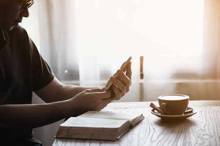 Man using mobile phone while drinking coffee and reading book in coffee shop - modern life style people in coffee shop conceptの写真素材