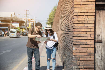 Asian backpack couple tourist holding city map crossing the road - travel people vacation lifestyle...