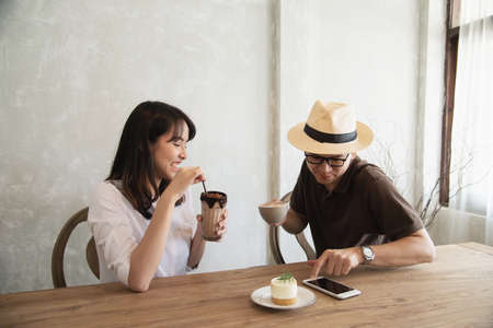 Casual man and woman talking happily while drink coffee and looking mobile phone - happy time lifestyle in coffee shopの写真素材