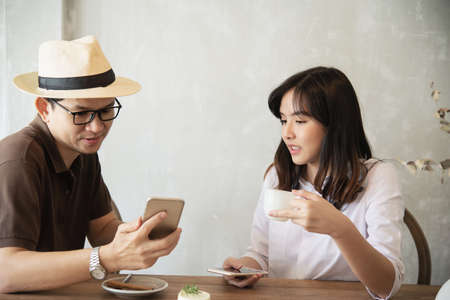 Casual man and woman talking happily while drink coffee and looking mobile phone - happy time lifestyle in coffee shopの写真素材