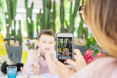 Mom use mobile phone take a photo of her son in restaurant - family lifestyle mother and son enjoy...