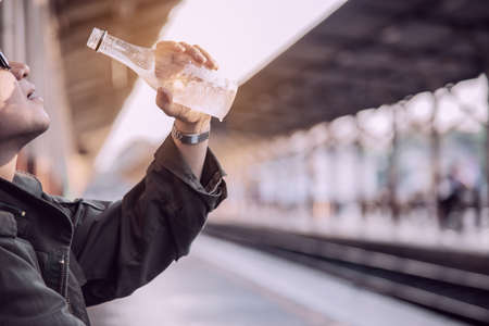 Travel man drink water while waiting train at platform - people vacation lifestyle activities at train station transportation conceptの写真素材
