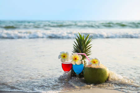 Cocktail glasses with coconut and pineapple on clean sand beach - fruit and drink on sea beach backgroudn conceptの写真素材