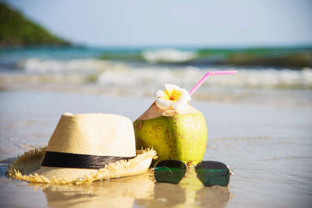 Fresh coconut with hat and sun glasses on clean sand beach with sea wave background - fresh fruit...