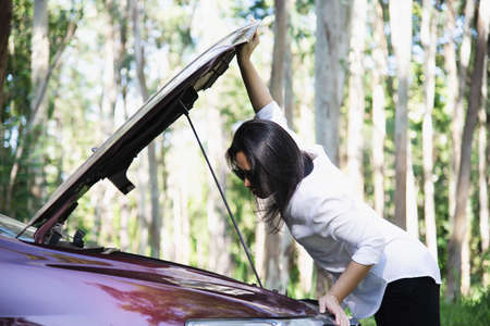 Asian woman calling repairman or insurance staff to fix a car engine problem on a local road - people with car problem transportation conceptの写真素材