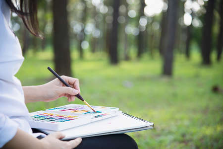 Relax woman painting water colour art work in green garden forest nature - people with creative art in nature stress reduction and meditation conceptの写真素材