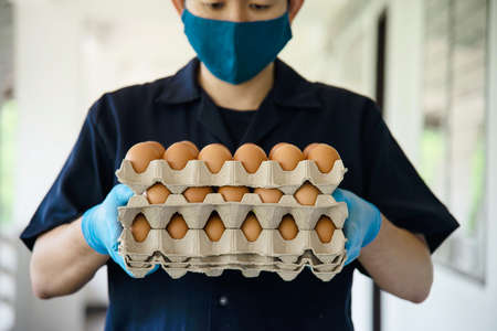A man carry 3 layers eggs tray for stay safe at home putting sanitary glove during corona virus COVID-19 spreading - people keeping food in COVID-19 viral spread period concept.の写真素材