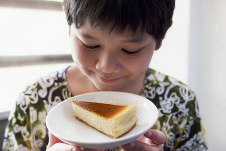 Smiling boy holding New York cheesecake happily - people with homemade cooking bakery conceptの写真素材