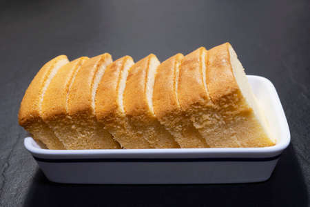 Homemade sliced butter cake in white ceramic tray over black background - famous homemade cake...
