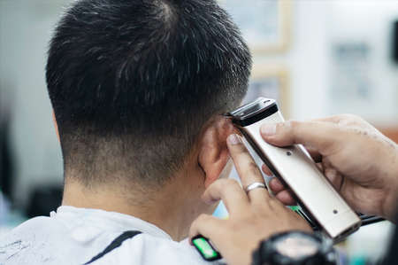 Man is cut his hair in barber shop - people in hairdresser beauty salon concept