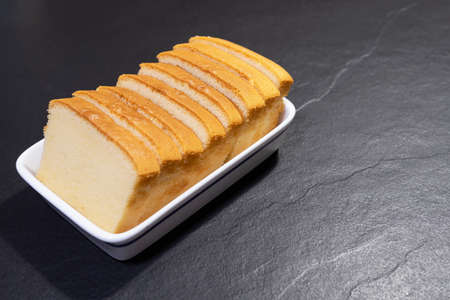 Homemade sliced butter cake in white ceramic tray over black background - famous homemade cake...