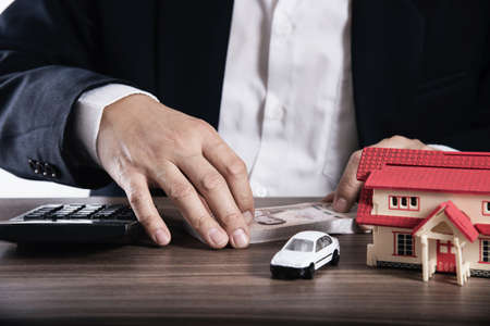 Business man is using calculator thinking about money for house and car payment - people with real estate financial insurance conceptの写真素材