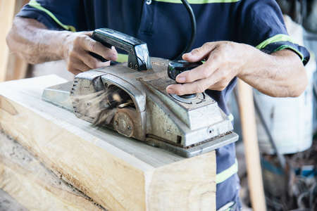 Carpenter man is using electrical wood planer machine working with wood construction item