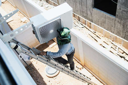 Man is installing wall compressor of air conditioner during hot seasonの写真素材