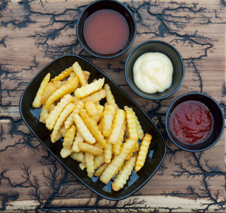 Side view of French fries with sauces on wood plate