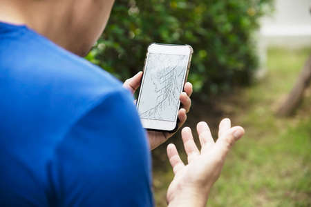 Man holding broken mobile with damaged displayの写真素材