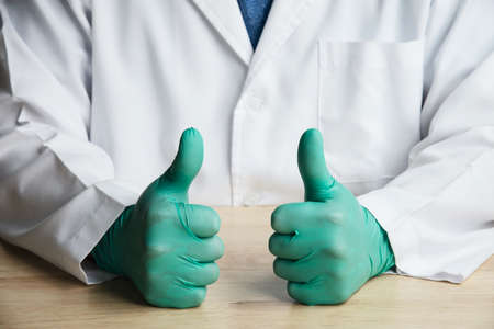 Middle part of doctor sitting and put green glove showing thumb up cheer signの写真素材