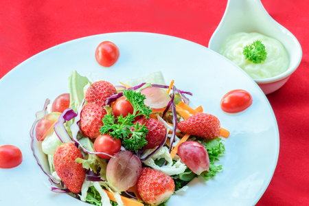 thai fruits salad topping with tomato on white plate and salad dressing on red backgroundの写真素材