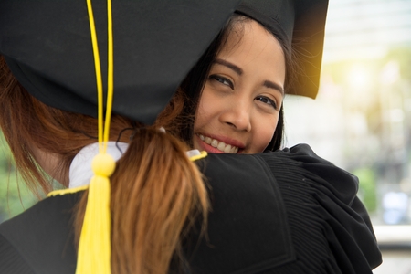 Portrait of successful graduate female student wearing cap and gown holding diplomaの写真素材