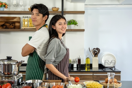 Portrait of cute happy couple in aporn jposting to prepare breakfast decorated with salad in modern kitchen and having a good timeの写真素材