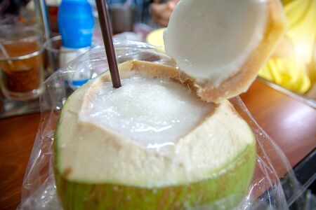 Coconut juice smoothie put within coconut fruit is placed for refreshment with straw.  .Sweet coconuts juice smothie water with drinking straw on wooden board. Coconut tropical fruit in Thailandの写真素材
