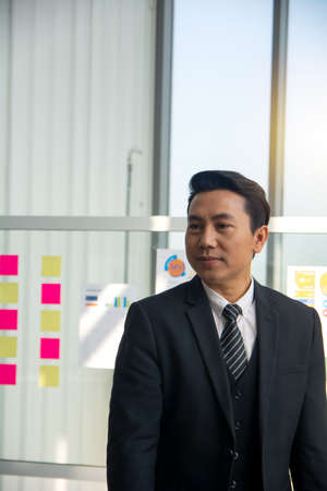 Confident attractive caucasian stylishly dressed guy, ceo, freelancer or employee, standing near window,  and smiling friendly in cosy officeの写真素材