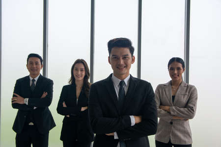 Successful businessman with crossed arms standing proudly in front his business team and looking at the camera.  A businessman standing out of and backup by profession team. Selective focus on man in front.の写真素材