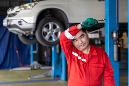 Hot and tired man professional mechanic repairs car in garage. Car maintenance and auto service garage concept. Closeup hand and spanner. Selective Focus.の写真素材