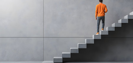 A person in an orange sweater climbs a modern staircase with a sleek gray background, embodying determination.の素材