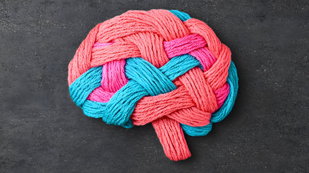 This image features a brain-shaped design crafted from brightly colored threads, predominantly pink and blue, set against a textured dark background, showcasing creativity and imagination.の素材