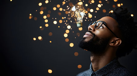 A man with glasses gazes upward, captivated by a glowing light bulb surrounded by shimmering, soft sparks, creating a magical atmosphere evoking creativity and inspiration.の素材