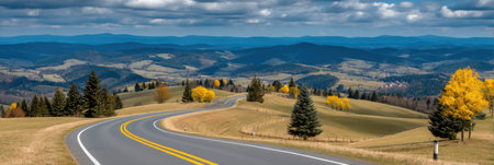 A beautiful winding road meanders through a stunning autumn landscape, showcasing vibrant foliage and rolling hills under a dramatic sky.の素材