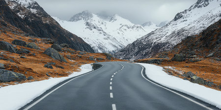 Captivating image of a winding road through majestic mountains, showcasing snow-capped peaks under a moody sky, perfect for travel and nature themes.の素材