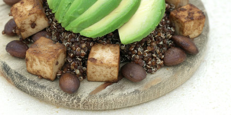A vibrant and healthy quinoa salad featuring creamy avocado, seasoned tofu, and crunchy cocoa nibs, beautifully presented on a rustic wooden plate.の素材