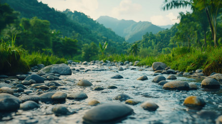 A crystal-clear river flows gently over smooth stones, surrounded by vibrant greenery and majestic mountains. This tranquil scene captures the essence of natural beauty and serenity.の素材